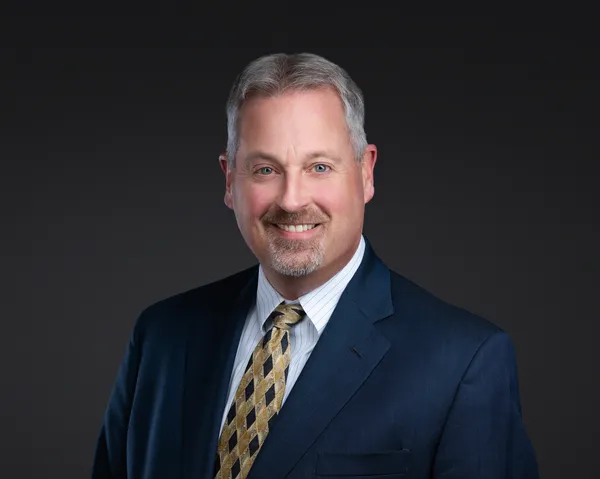 Executive headshot of a man in a navy blazer and tie
