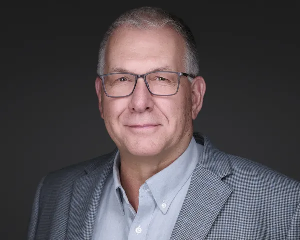 Executive headshot of a man with gray hair in a dark jacket