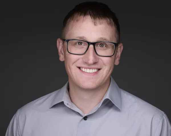 Corporate headshot of a man in glasses and a dark shirt