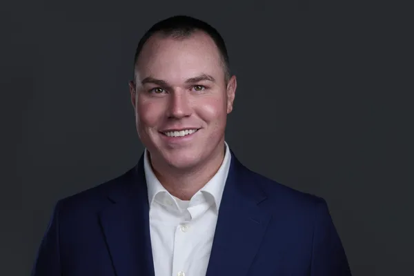 Headshot of a man in a navy quarter-zip on a dark background